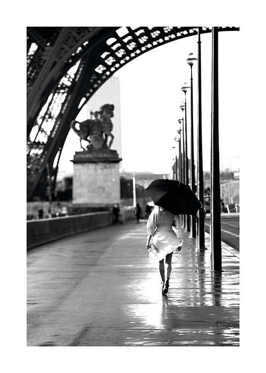  – Black and white photograph of a woman walking with an umbrella underneath the Eiffel Tower