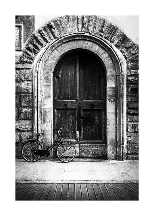  - Black and white photograph of a rustic door with a bike in front of it